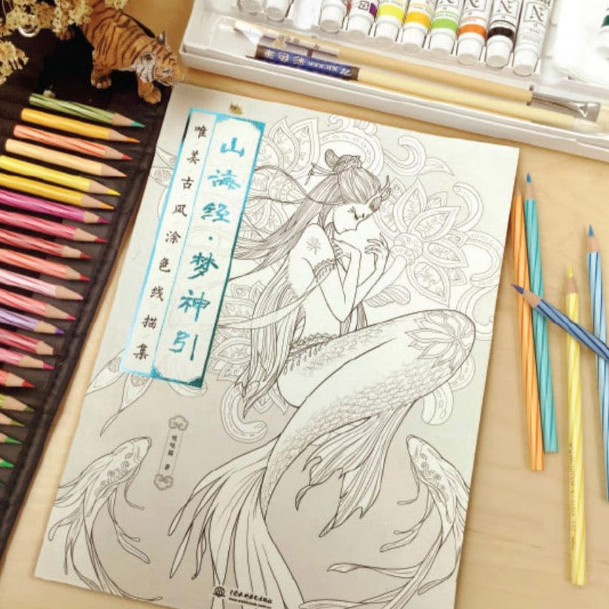 Chinese God and Goddess Adult Coloring Book on a table with colorful pencils, paintbrushes, and tubes of paint.