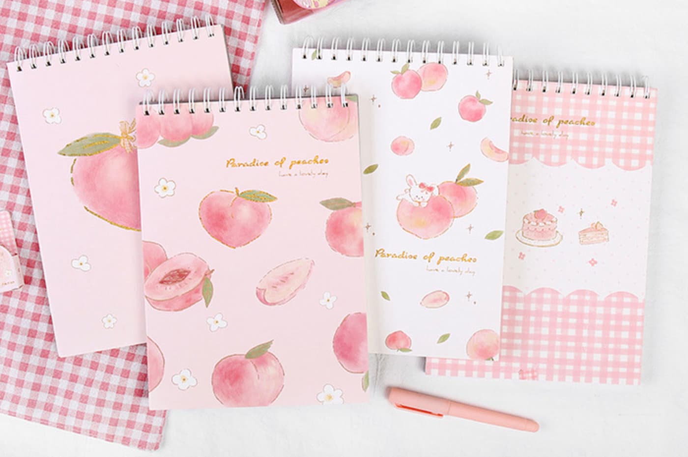 A4 Pink Peach Coil Sketch Book - Cute Planner with adorable peach-themed covers, perfect for kawaii stationery enthusiasts, includes peach illustrations, gingham patterns, and a pink pen on a checkered cloth background.