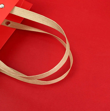 Close-up of a red Christmas paper gift bag with sturdy beige handles, featuring a festive Santa Claus design.