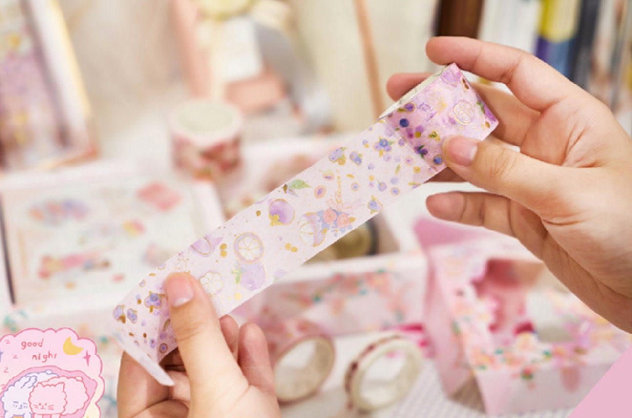 Red Fruit Washi Tape Set for Bullet Journals, featuring hands holding a roll of decorative tape with cute, colorful fruit and floral designs.