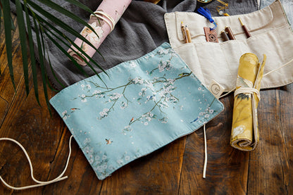 Floral roll-up pencil case and artist brush holder with a light blue background and delicate white cherry blossom print, aesthetic and kawaii stationery organizer on a wooden table.