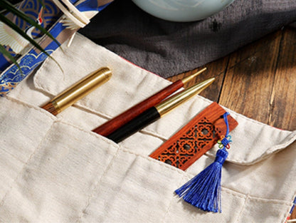 Floral roll-up pencil case and artist brush holder with beige pockets, holding pens, brushes, and a wooden bookmark with a blue tassel.