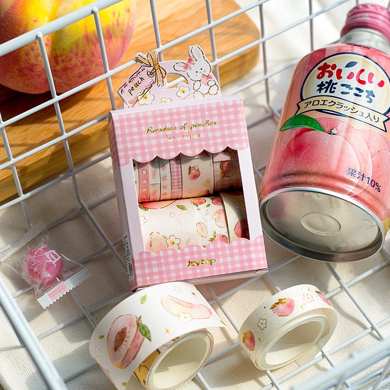 Peach Pink Washi Tape Set - 10 Rolls featuring cute peach and floral designs in a pink checkered box, displayed with a peach drink and whole peach in background. Kawaii stationery.