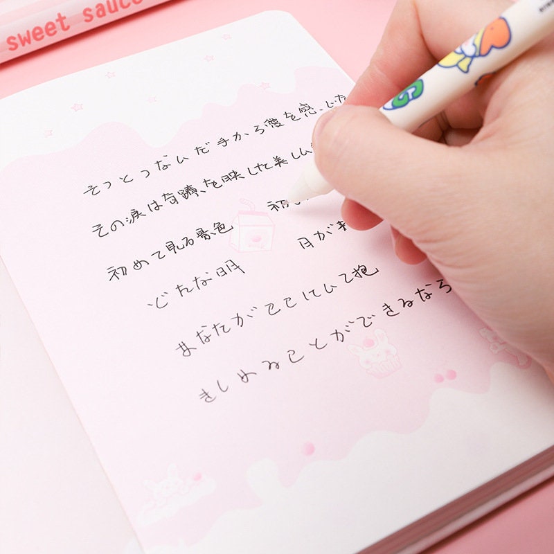 Hand writing in a Sweet Cherry Leather Journal with pink kawaii design, featuring Japanese text and cute illustrations, A5 planner with magnetic buckle.