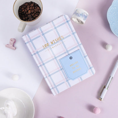 Hard Cover A5 Minimalist Grid Pocket Planner with plaid design, surrounded by coffee beans, a pen, washi tape, and a pink paper clip on a pastel background.