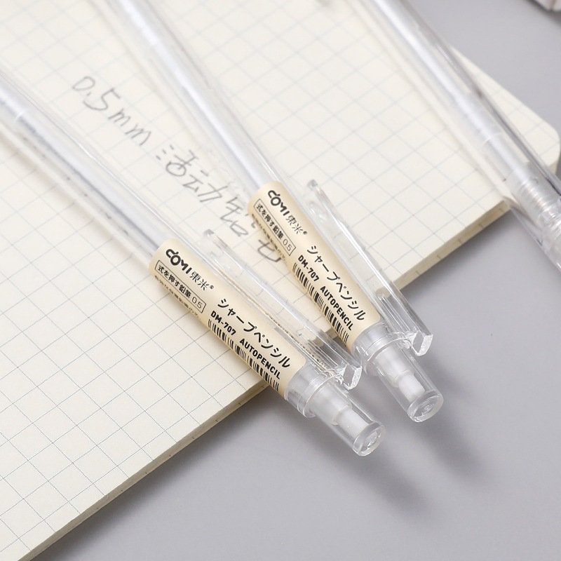 0.5mm transparent mechanical pencils on grid notebook - ideal for office and student stationery needs.