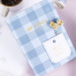 Hard Cover A5 Minimalist Grid Pocket Planner with blue checkered design, "100 Wishes" in gold text, white pocket labeled "secret in my pocket," next to a cup of coffee and dried flowers.