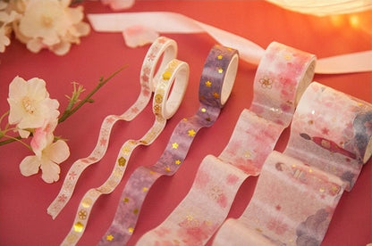 Japanese Cherry Blossom Washi Tape Set - 6 Rolls, featuring pastel pink, purple, and white tapes with delicate floral and gold foil accents, displayed on a pink background with cherry blossom flowers. Perfect for decorating planners, journals, and crafts.