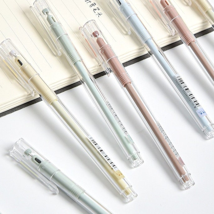 0.5mm minimalist black ink gel pens with clear caps and colorful barrels, ideal for office use, displayed on a white desk next to an open notebook.