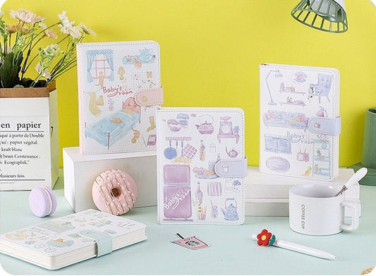 Purple Blue Leather Journal - Magnetic Buckle Planner with kawaii illustrations of baby room scenes, surrounded by cute stationery items on a pastel-colored desk setting.