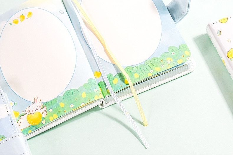 Magnetic Buckle Leather Planner - Lemon Girl Design featuring cute interior artwork with a rabbit holding a lemon on a meadow background, lemon-themed illustrations, and pastel-colored ribbon bookmarks.