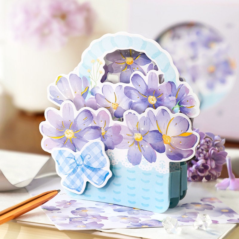 3D pink flower pop-up greeting card featuring rose and lily in a pastel-colored floral basket with a blue bow.