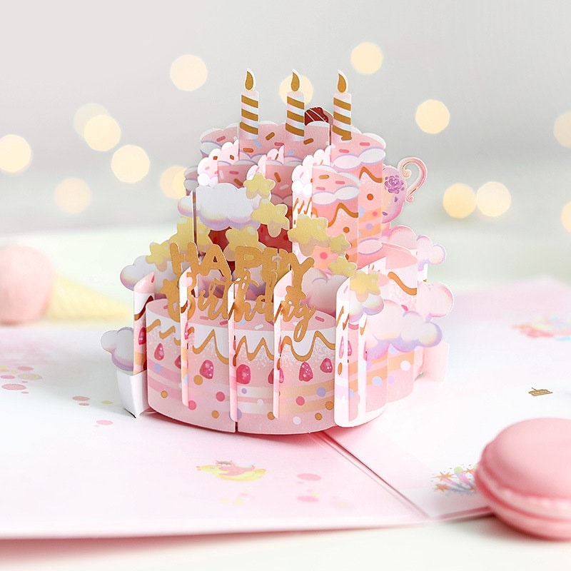 3D Pink Cake Pop Up Card - Happy Birthday with intricate design featuring layers of pink cake, candles, and elegant gold "Happy Birthday" lettering. Kawaii style birthday card with pastel colors and cute details, perfect for a special celebration.