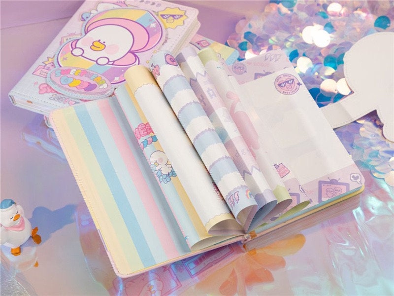 Soya Duck Leather Notebook A5, 224 Pages - Opened kawaii notebook with pastel-colored pages and cute Soya Duck illustrations on a reflective surface with confetti background.