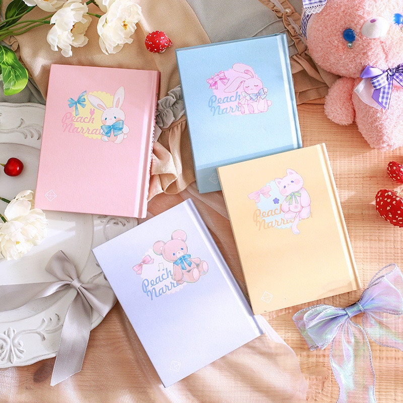 Peach Narration Magnetic Buckle Journal with Bookmark in Pink, Blue, Yellow, and Lavender Featuring Cute Animal Illustrations and Bow Decor on a Decorative Table Setting