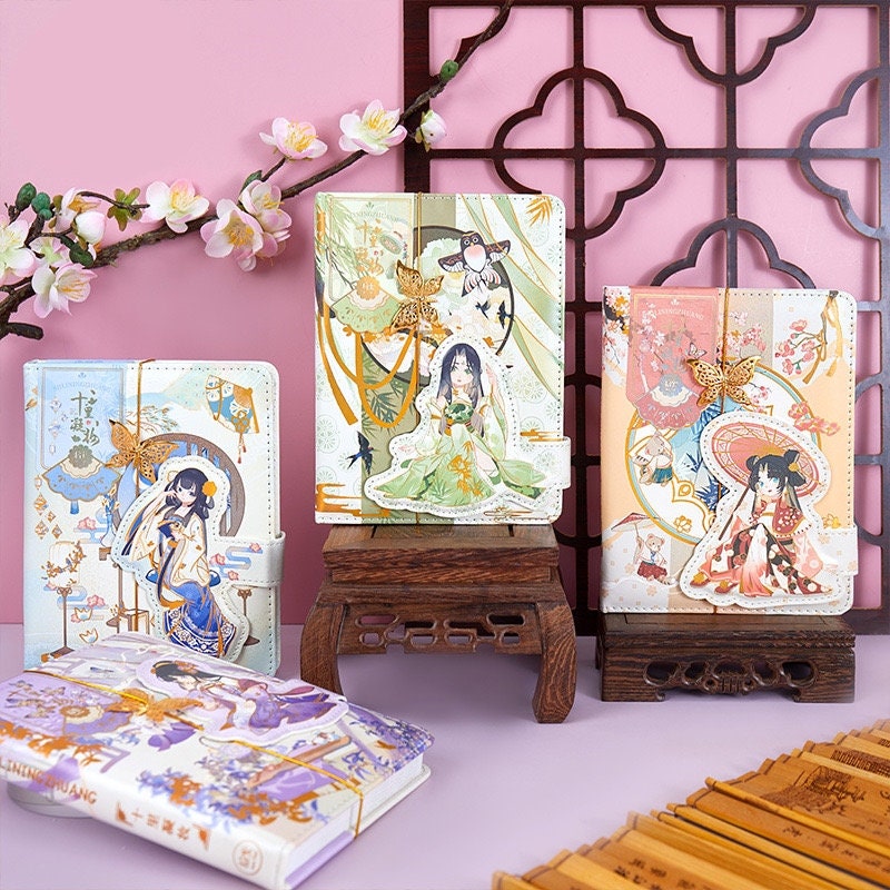 Butterfly Leather Journal with Metal Bookmark featuring kawaii style illustrations, displayed alongside decorative items with cherry blossoms against a pink background.