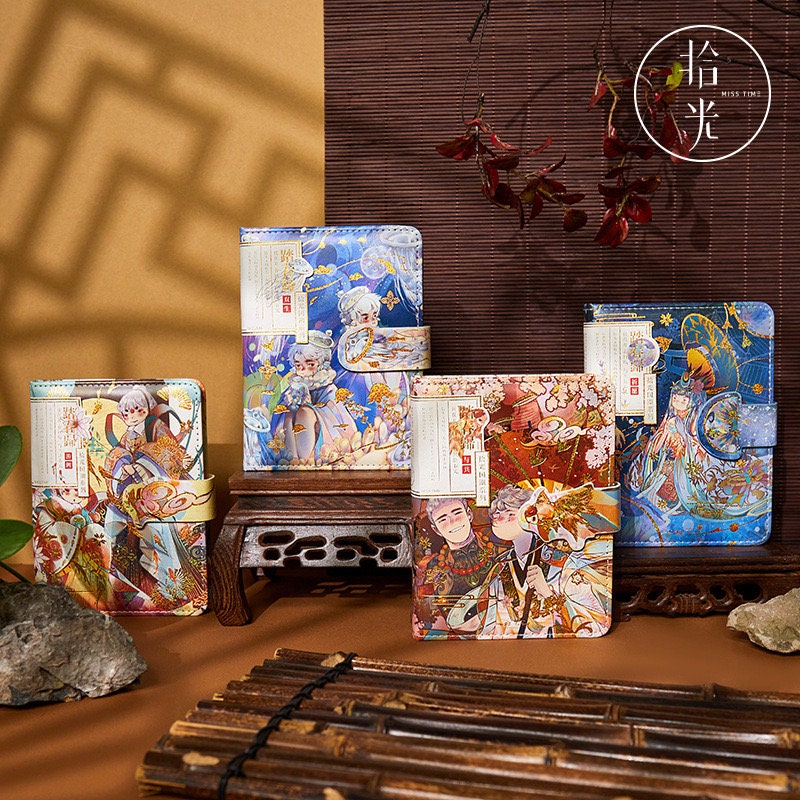 Gold foil anime boy journals with magnetic leather buckle in vibrant, artistic designs, displayed on a traditional wooden table against a warm background.