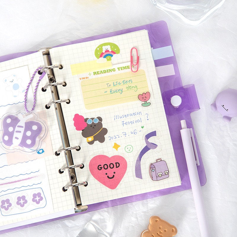 A6 Loose Leaf Planner with Stickers and Cards, featuring cute kawaii designs, colorful illustrations, and various decorative stickers, organized in a purple binder with a white pen and additional accessories.