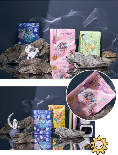 Spaceship Leather Journal with Bookmark - Magnetic Buckle, cute kawaii design with astronaut and space-themed illustrations in pink, blue, and green. Perfect for notes and drawings, surrounded by rocks and astronaut figurine.