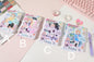 NANA Campus Stars A6 Leather Notebook with Bookmark in four design variations (A, B, C, D) featuring cute anime-style characters and pastel colors, displayed on a pastel pink desk with kawaii stationery items including washi tapes, pens, and a heart-shaped sticker.