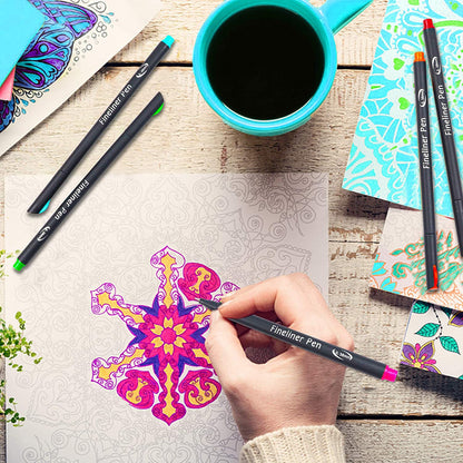 Person using a 48 color fineliner pen to color a detailed and intricate mandala design, surrounded by various colored fineliner pens, colorful journals, and a blue coffee cup.