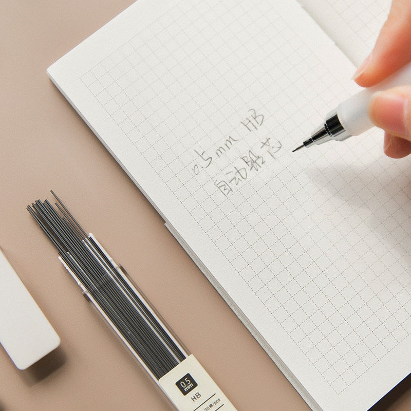 0.5mm mechanical pencil refill pack with 20 count HB leads, shown beside a hand writing on a grid notebook.