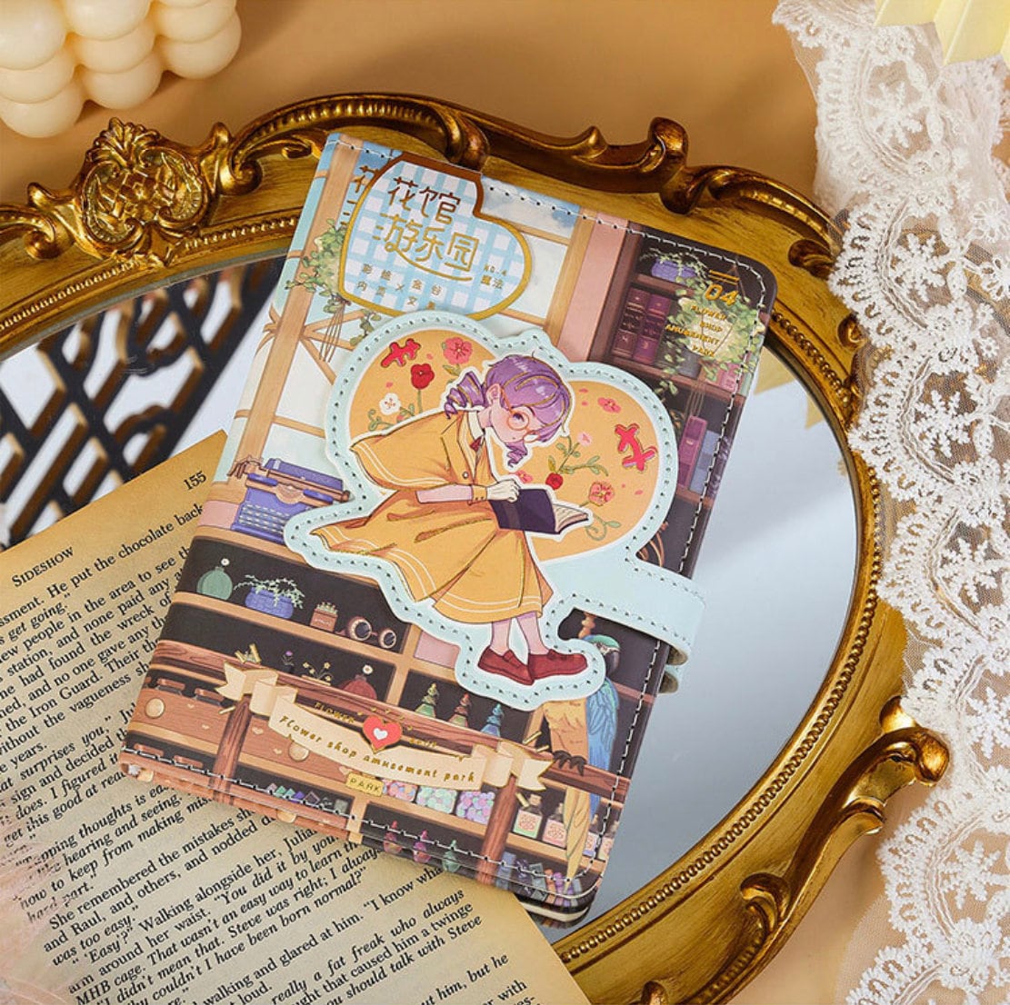 Blue Flower House Leather Journal - A6, 192 Pages, featuring a cute illustrated girl reading a book on a floral-themed cover with vintage aesthetic, displayed on a gold frame mirror with lace accents.