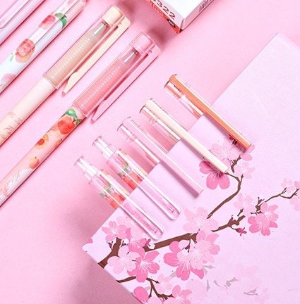 Peach scented kawaii gel pens with 0.5mm tip, featuring adorable peach designs, arranged on a pink sakura diary background.