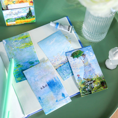 Sunset Wave Sticky Notepad with Stand - 60 Pages, featuring colorful designs inspired by nature and art, displayed on an open book with a mint green pen and decorative items on a green surface.