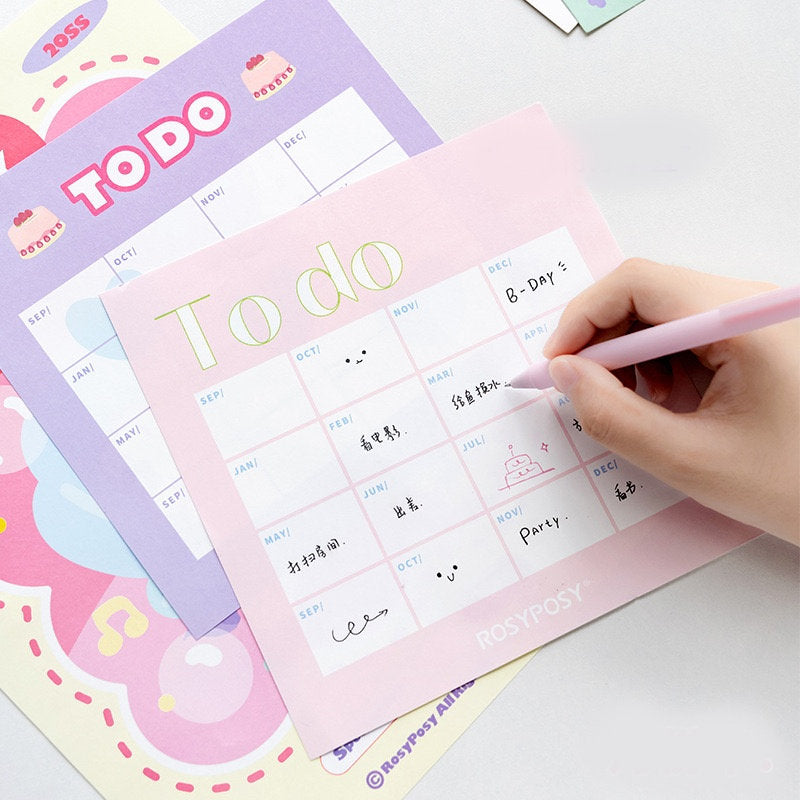 2022 Goal Tracker Calendar with Stickers in kawaii style with pastel colors and cute illustrations, showing hands writing on the calendar with a pink pen.