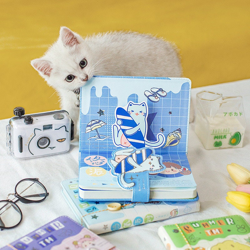 Magnetic Buckle A5 Hard Cover Summer Journal with adorable cat illustrations surrounded by cute stationery items including a cat-themed camera, glasses, and avocado milk container.