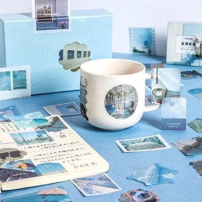 80-piece washi paper sticker set for mood board decor, featuring assorted blue-themed designs, displayed alongside a white mug and an open notebook with journaling.