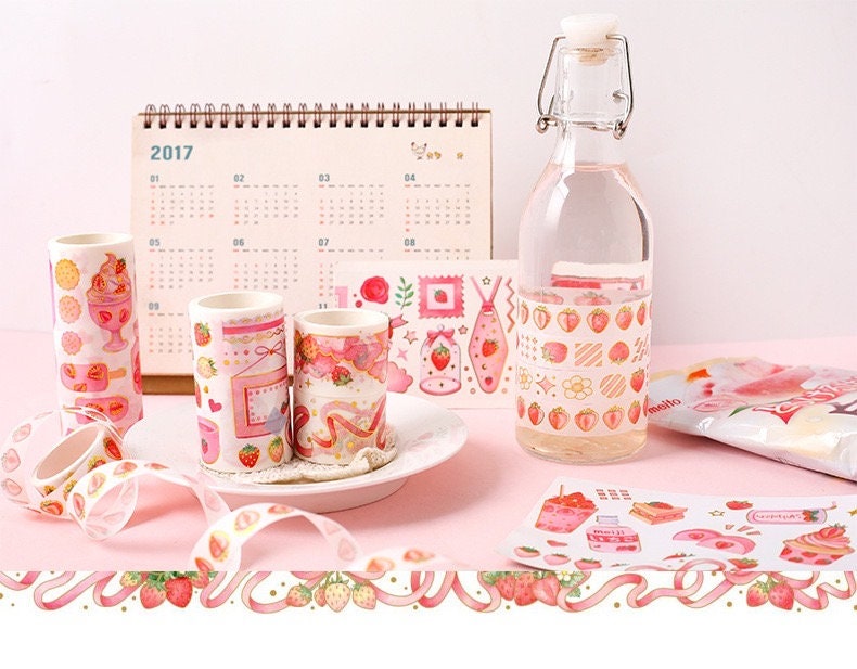 Strawberry Washi Tape Roll for Parties and Crafts, displayed with kawaii-style stationery on a pink surface, including decorative items and a 2017 calendar.