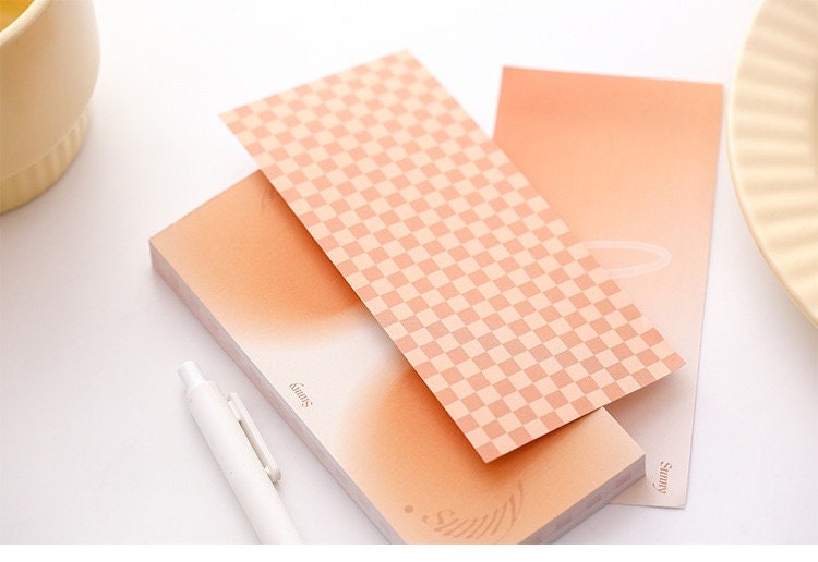 Dreamy Island Notepad Set featuring 90 sticky notes with pastel peach gradient and checkerboard designs, accompanied by a white pen.