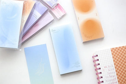 Dreamy Island Notepad Set featuring 90 sticky notes in pastel designs, including blue and peach tones, laid out on a white surface with additional stationery items.