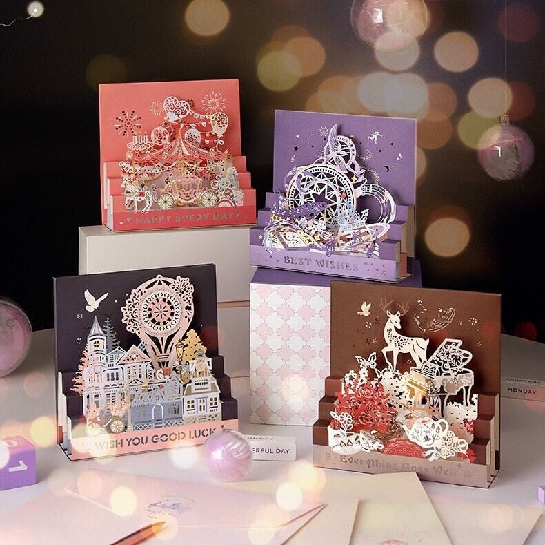 Starlight Studio Pop Up 3D Greeting Card featuring intricate designs, including a pink carnival scene with "HAPPY EVERYDAY" text, a purple dreamy night with "BEST WISHES" text, a brown woodland with a deer and "Everything goes well" text, and a detailed town with a Ferris wheel and "WISH YOU GOOD LUCK" text. Perfect for special occasions and celebrations.