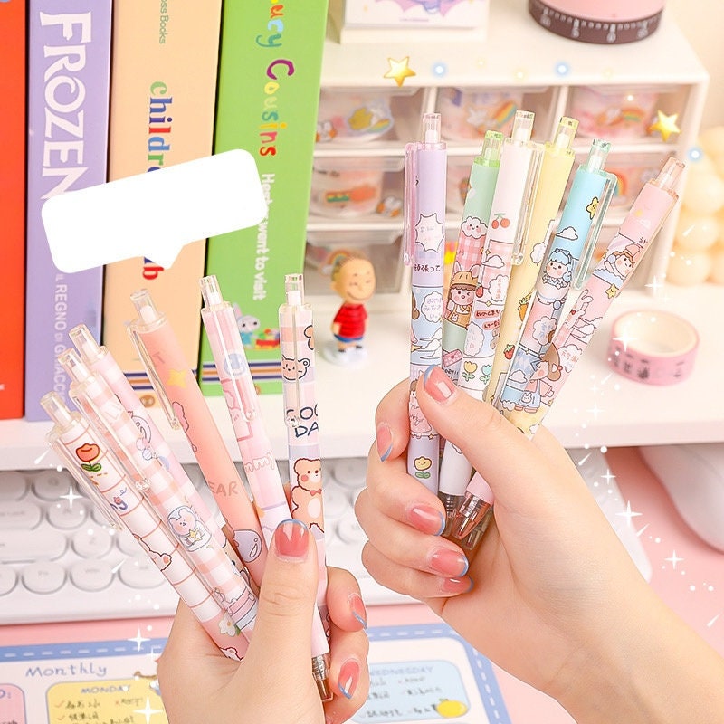 Kawaii Girl Gel Pen Set - 0.5mm Black Ink featuring colorful, adorable designs, held in hands against a background of kawaii stationary and books.