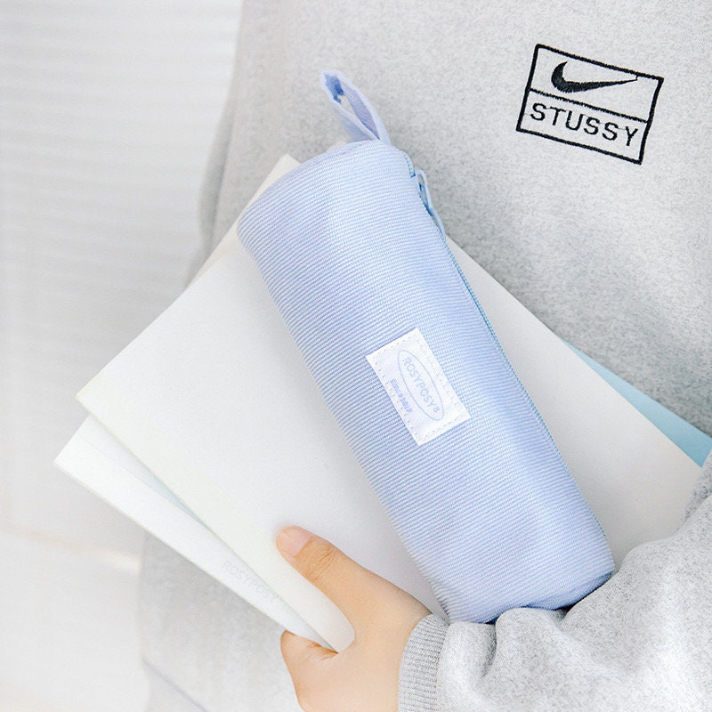 Double-sided milky cream fabric pencil case in light blue color held by a person wearing a gray sweater and carrying notebooks.