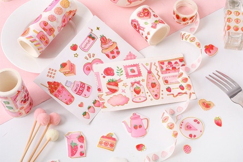 Strawberry Washi Tape Roll for parties and crafts featuring cute strawberry designs and pink-themed patterns arranged on a table with decorative stickers and craft supplies.