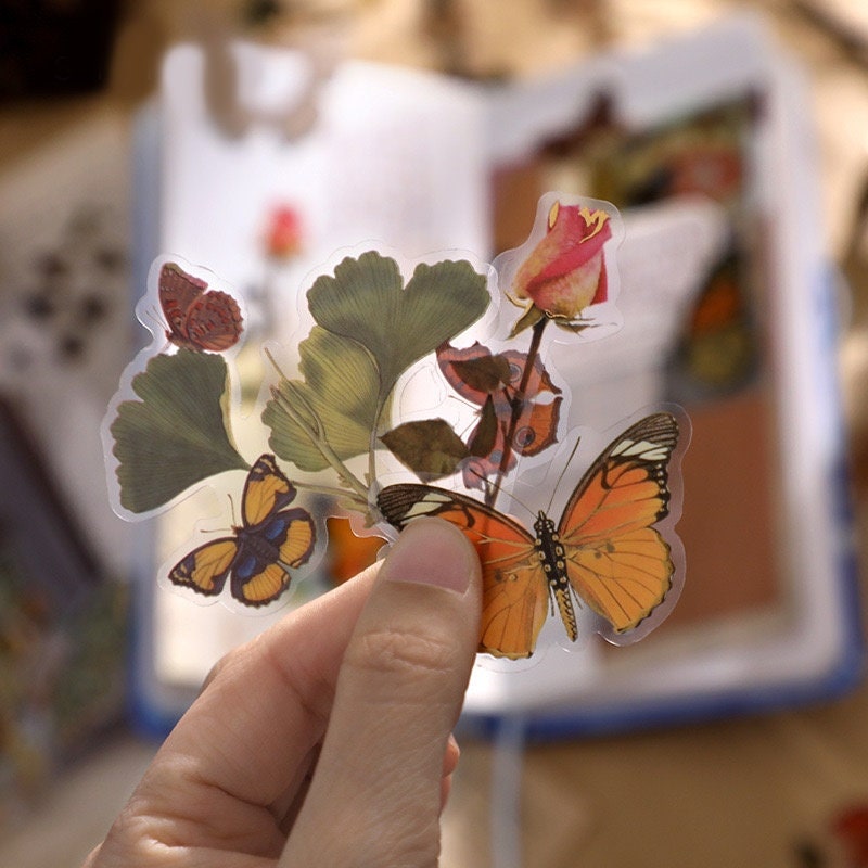 Hand holding flower and butterfly stickers from the 25-Flower Sticker Set for planner and craft decor.