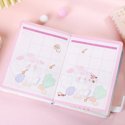 Peach leather notebook with bookmark, featuring a magnetic buckle, open to a pastel pink and white illustrated monthly calendar page with cute kawaii characters and star designs.