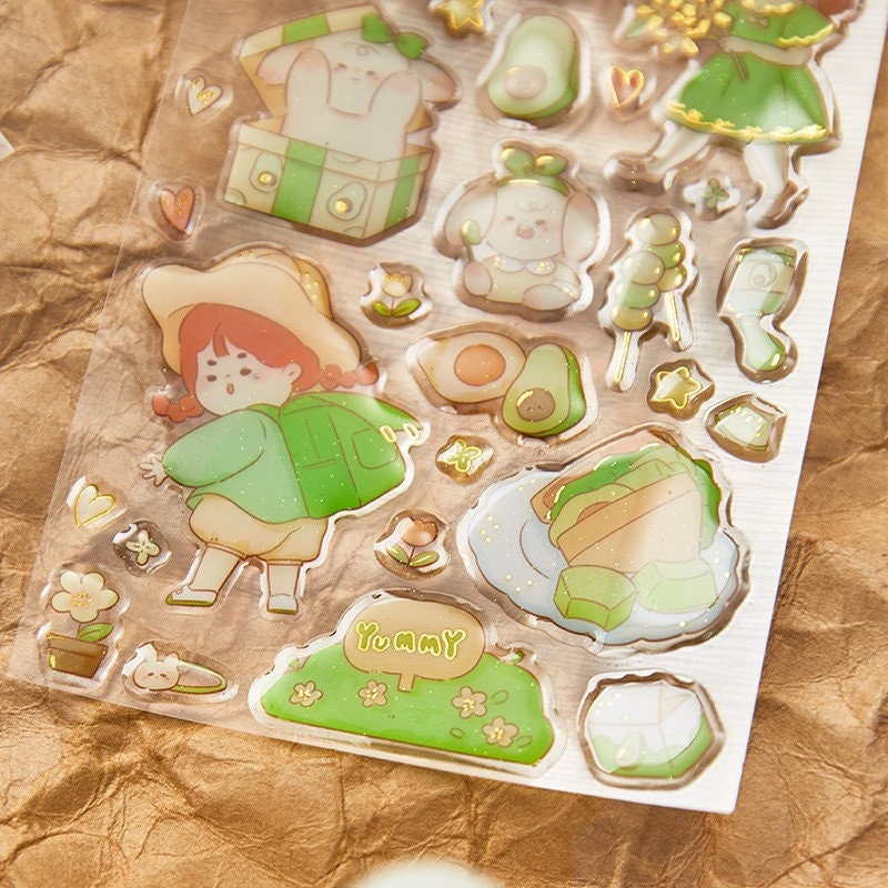 Kawaii gold foil jelly stickers featuring cute illustrations of a girl, animals, avocado, flowers, and sweet treats in pastel colors; perfect for crafts, DIY projects, and scrapbooking.