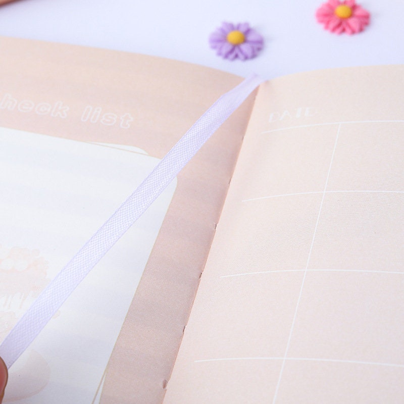 Open page of the Magnetic Buckle Flower House Leather Journal showing a white ribbon bookmark and pastel-colored pages with a check list and date section.