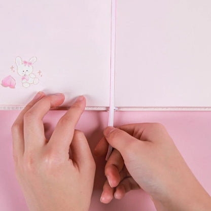 Hands holding the Peach Magnetic Buckle Leather Journal open to a page with a cute bunny and peach illustration.