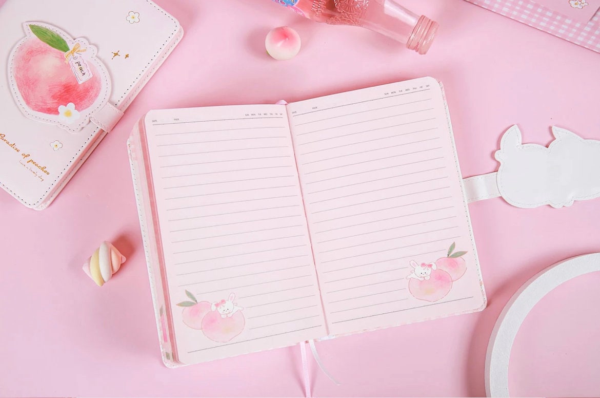 Peach Magnetic Buckle Leather Journal - 228 Pages with cute bunny and peach designs on soft pink pages, surrounded by pastel pink-themed stationery items on a pink background.