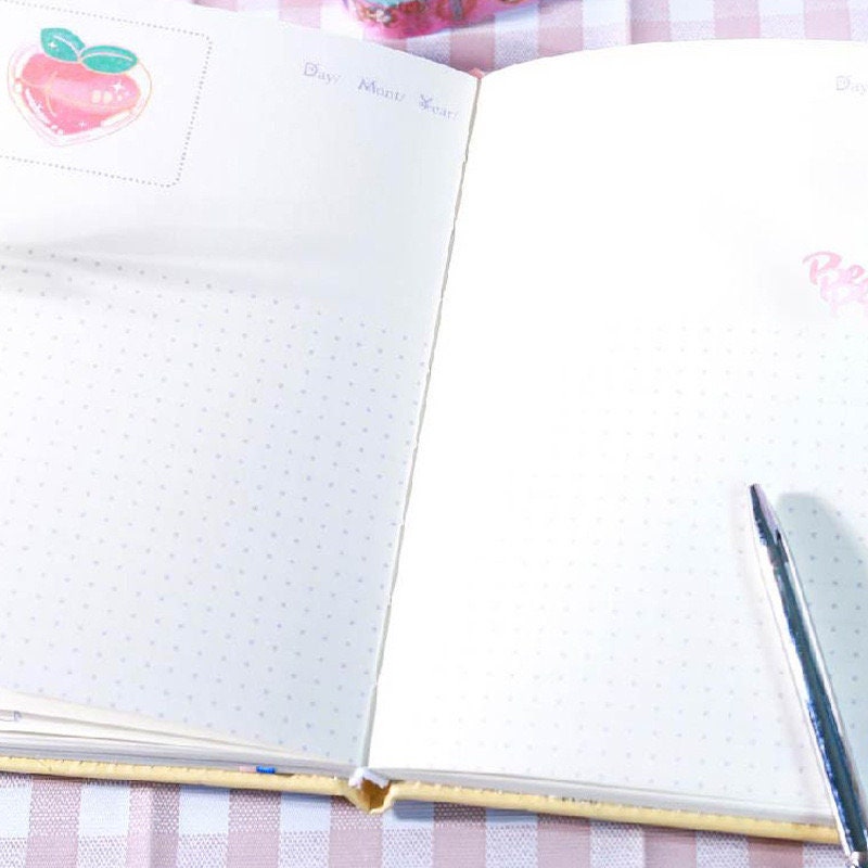 Otaku Girl Leather Journal with 3D Pages open on a checkered tablecloth, featuring dotted pages, a pen, and a cute peach sticker in the corner.