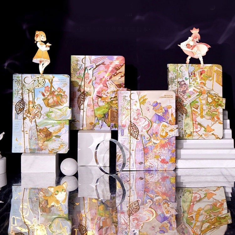 Anime hard cover journal with metal bookmark featuring cute and colorful illustrations, stacked on podiums with figurines.