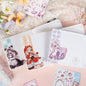 Poetry to the Snow Leather Journal with Bookmark featuring kawaii illustrations, surrounded by decorative stickers and pastel floral accents.