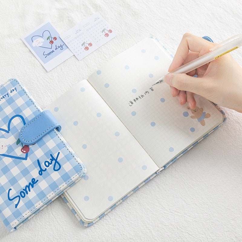 Magnetic Buckle Leather Grid Planner - Blue A6 Notebook with cute polka dots design, open to grid pages with a pen writing in it, next to cherry-themed page markers and cards, perfect for kawaii stationery lovers.