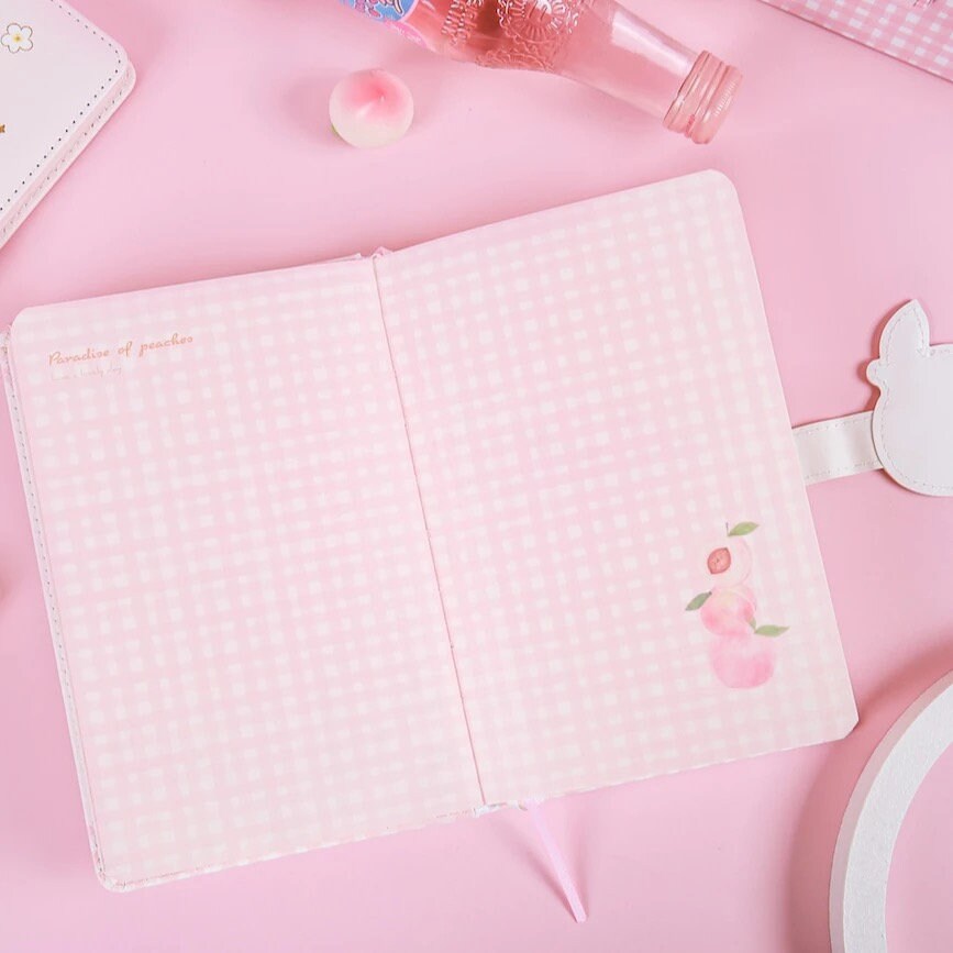 Peach Magnetic Buckle Leather Journal - 228 Pages, featuring pink checkered inner pages with peach illustrations and the phrase "Paradise of peaches", sleek kawaii stationery item, white leather magnetic buckle shaped like a bunny, ideal for cute and stylish note-taking.